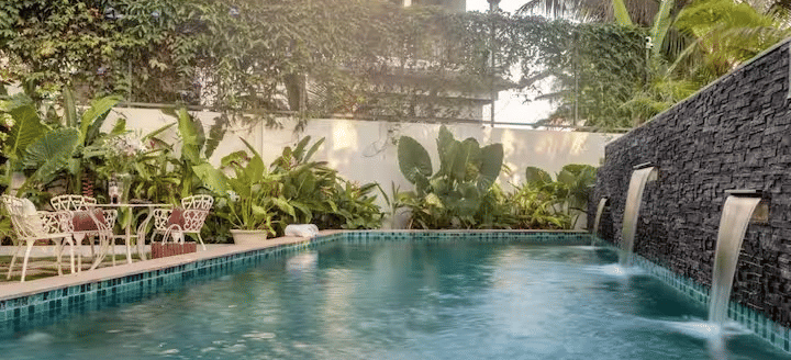 Swimming pool with a waterfall feature and lush plants surrounding the area at Lime Tree Villa with Private Pool | Luxury Stay in Goa.